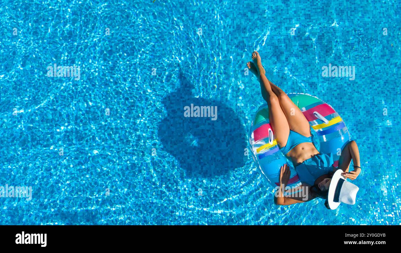 Belle fille dans le chapeau dans la piscine vue de dessus aérienne d'en haut, jeune femme se détend et nage sur anneau gonflable beignet et s'amuse dans l'eau Banque D'Images