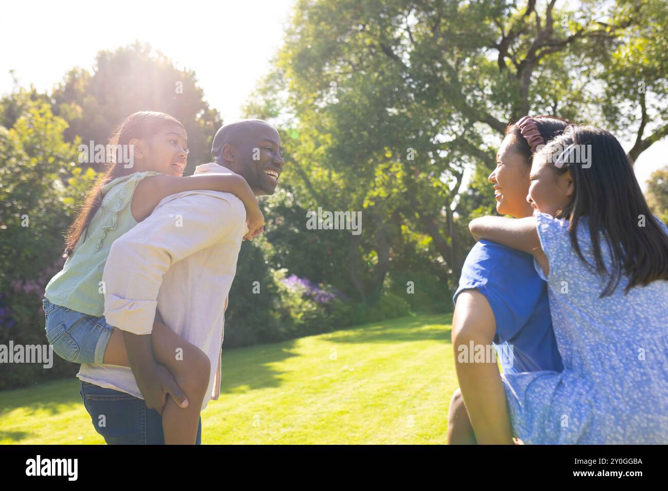 Porter des filles piggyback, parents multiraciaux souriants et profiter du temps en famille dans le parc ensoleillé Banque D'Images