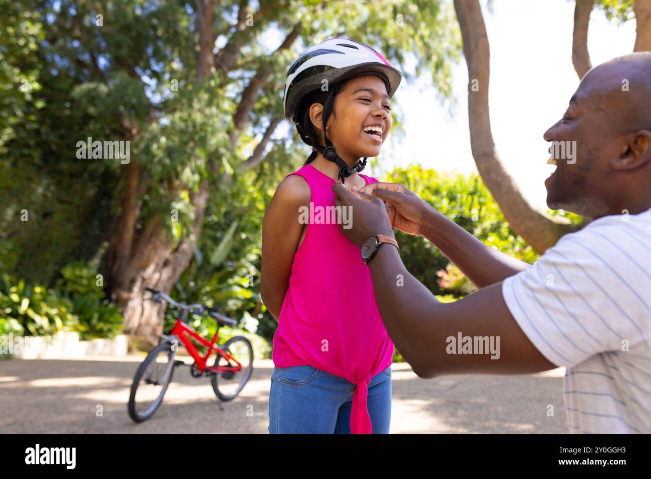 Père aidant la fille avec casque, se préparant pour la balade à vélo dans le parc Banque D'Images