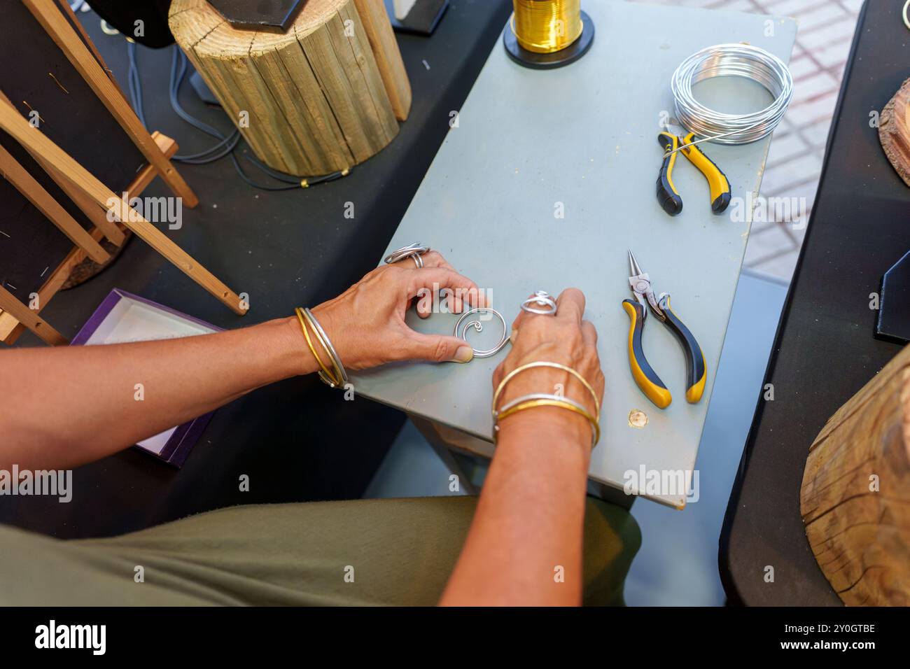 Femme hispanique méconnaissable dans ses années 50 Crafting boucles d'oreilles à son stand de rue vendant des bijoux en fil d'aluminium faits à la main Banque D'Images