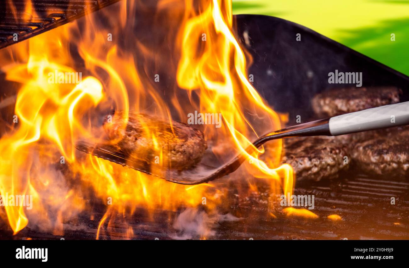 Cuisson de hamburgers sur un gril chaud avec des flammes - galettes hamburger de style barbecue dans la cour arrière grillées à la flamme. Les hamburgers sont un barbecue traditionnel d'été en plein air. Banque D'Images