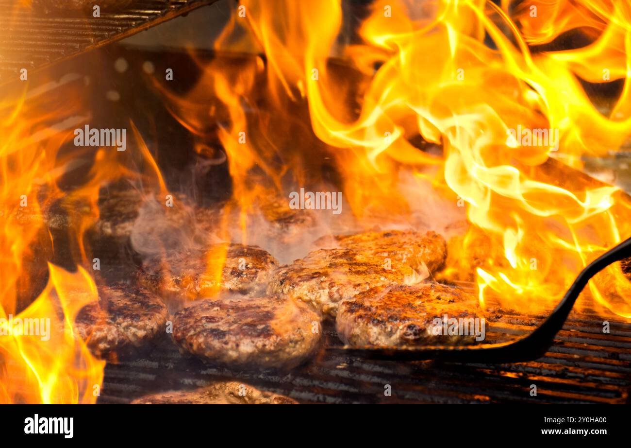 Cuisson des hamburgers sur un gril chaud avec des flammes - galettes hamburger grillées à la flamme. Les hamburgers sont un barbecue traditionnel d'été. Banque D'Images