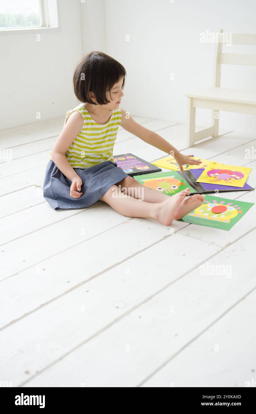 Fille assise sur le sol, touchant livre d'images Banque D'Images