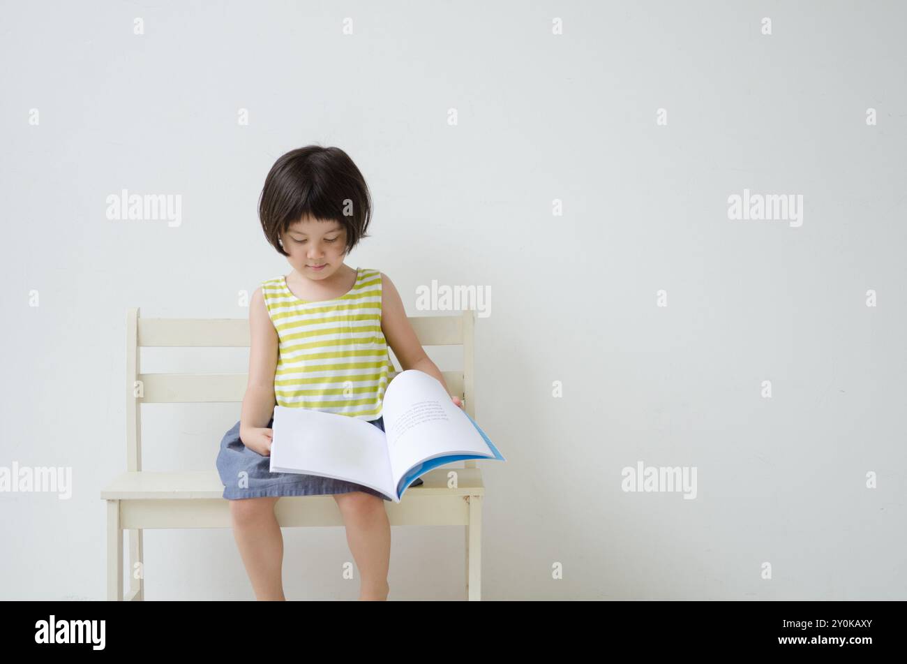 Fille tournant le livre d'images et assise sur un banc Banque D'Images