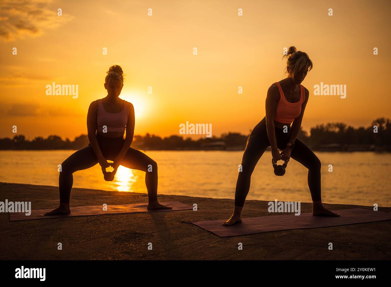 Deux femmes pratiquant le pilates avec kettlebell au coucher du soleil. Banque D'Images