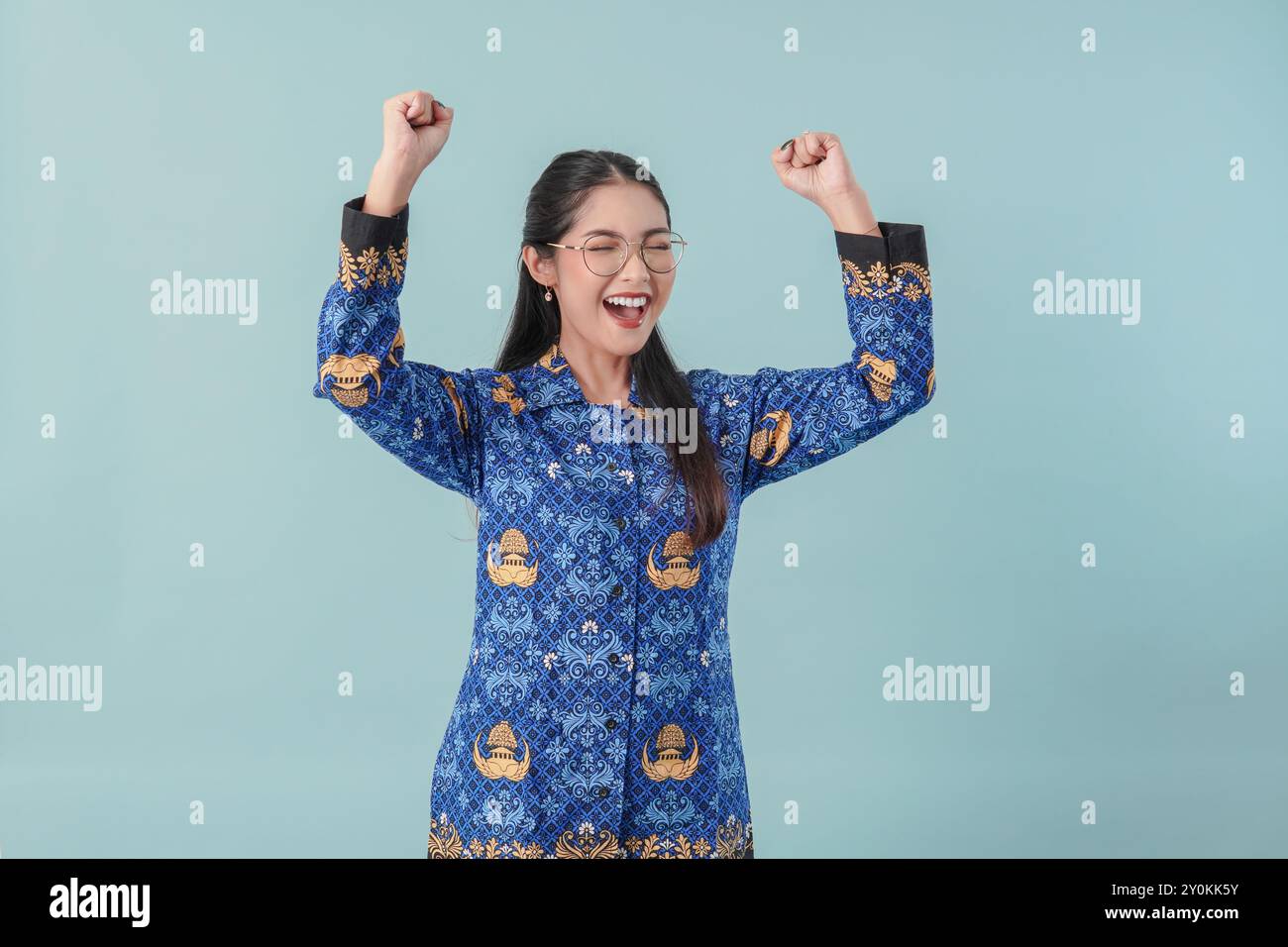 Femme travailleuse du gouvernement indonésien excitée portant un uniforme de batik bleu et des lunettes posant avec une expression heureuse et réussie. PNS concept de fonctionnaire Banque D'Images