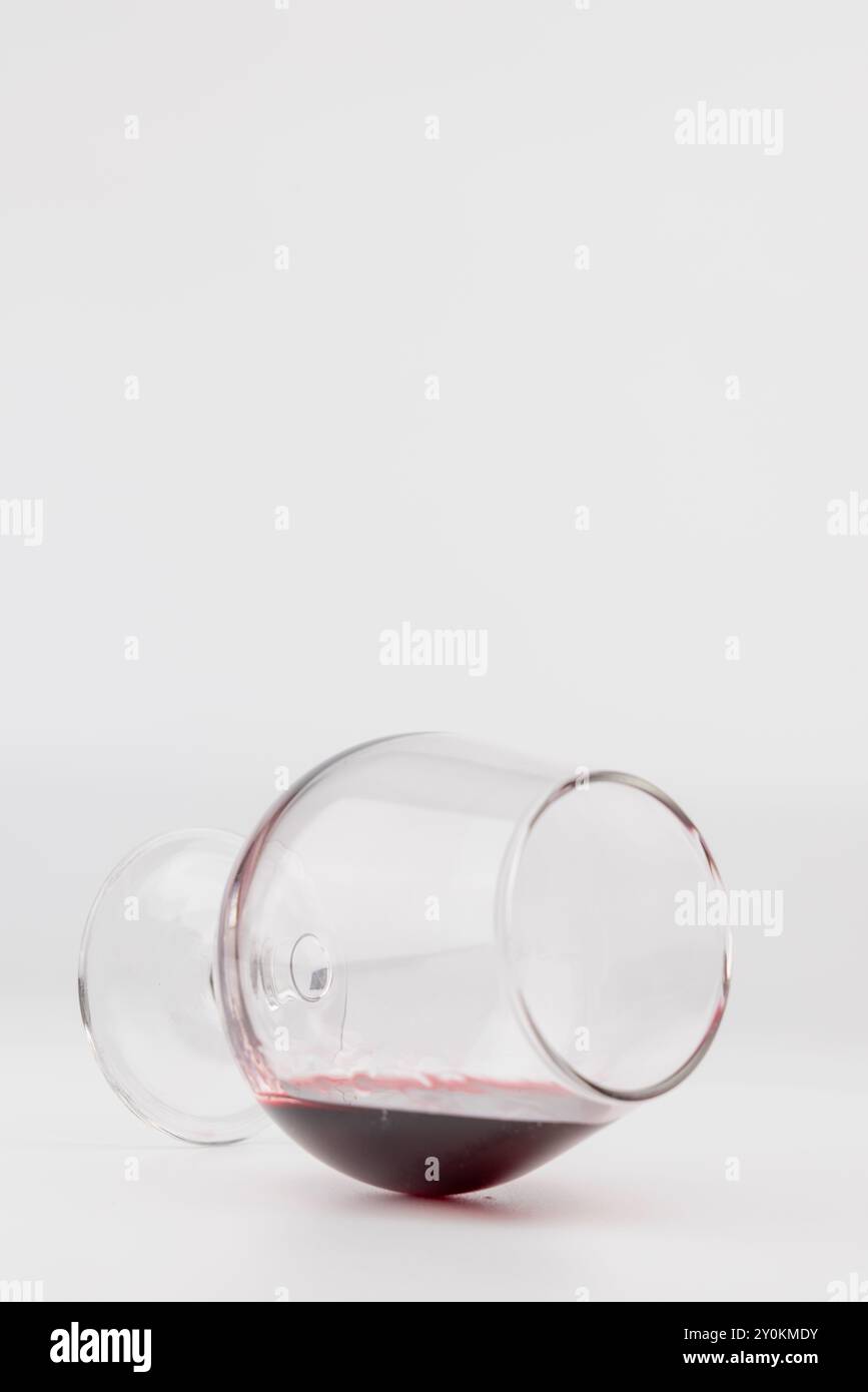 Une photo montrant un verre à vin renversé sur le sol, avec une petite quantité de vin rouge renversée sur une surface blanche. La vitre est positionnée sur la gauche Banque D'Images