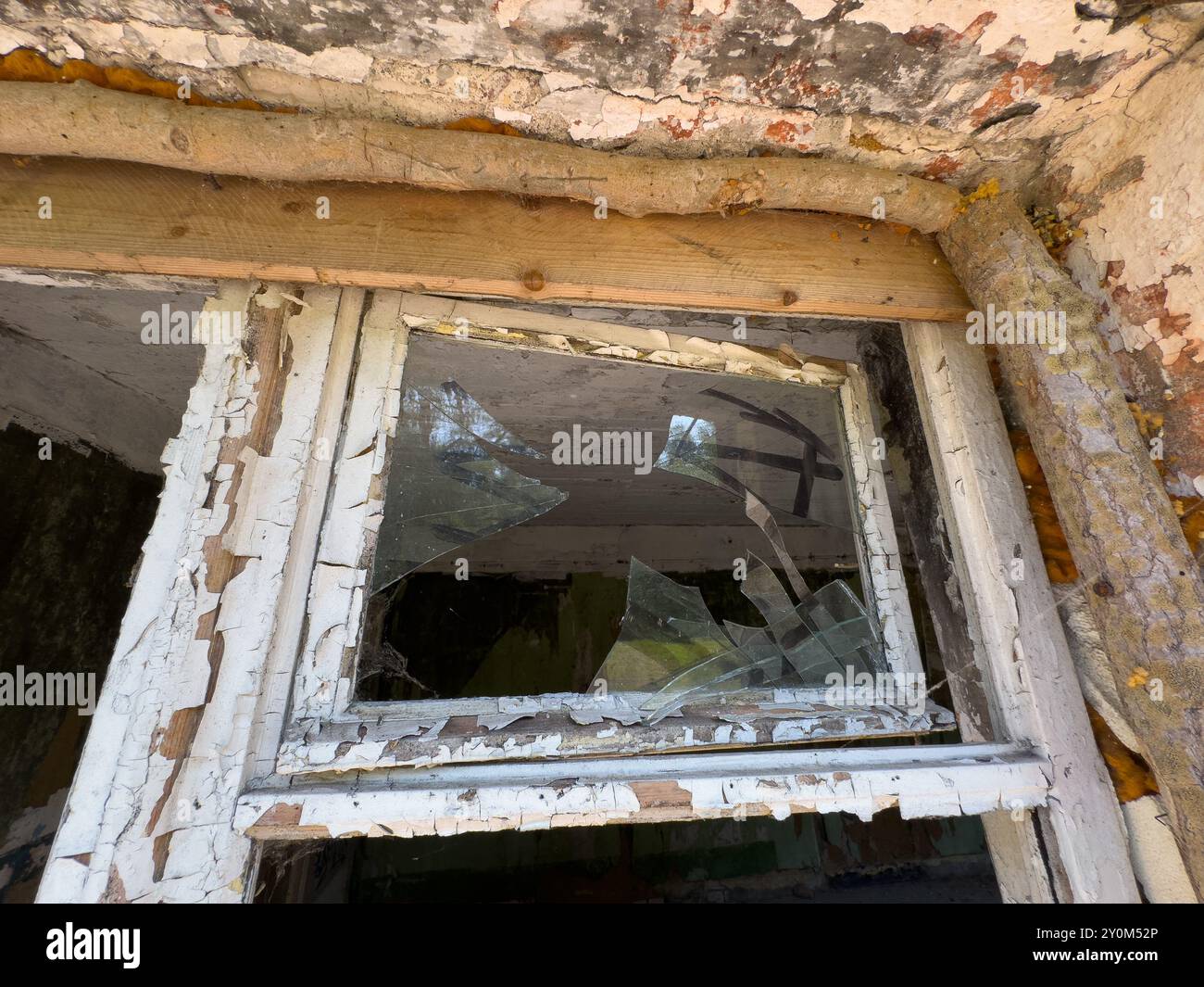 Gros plan d'une fenêtre brisée dans un vieux bâtiment abandonné. La peinture écaillée et le bois délabré suggèrent la négligence et la pourriture au fil du temps. Banque D'Images