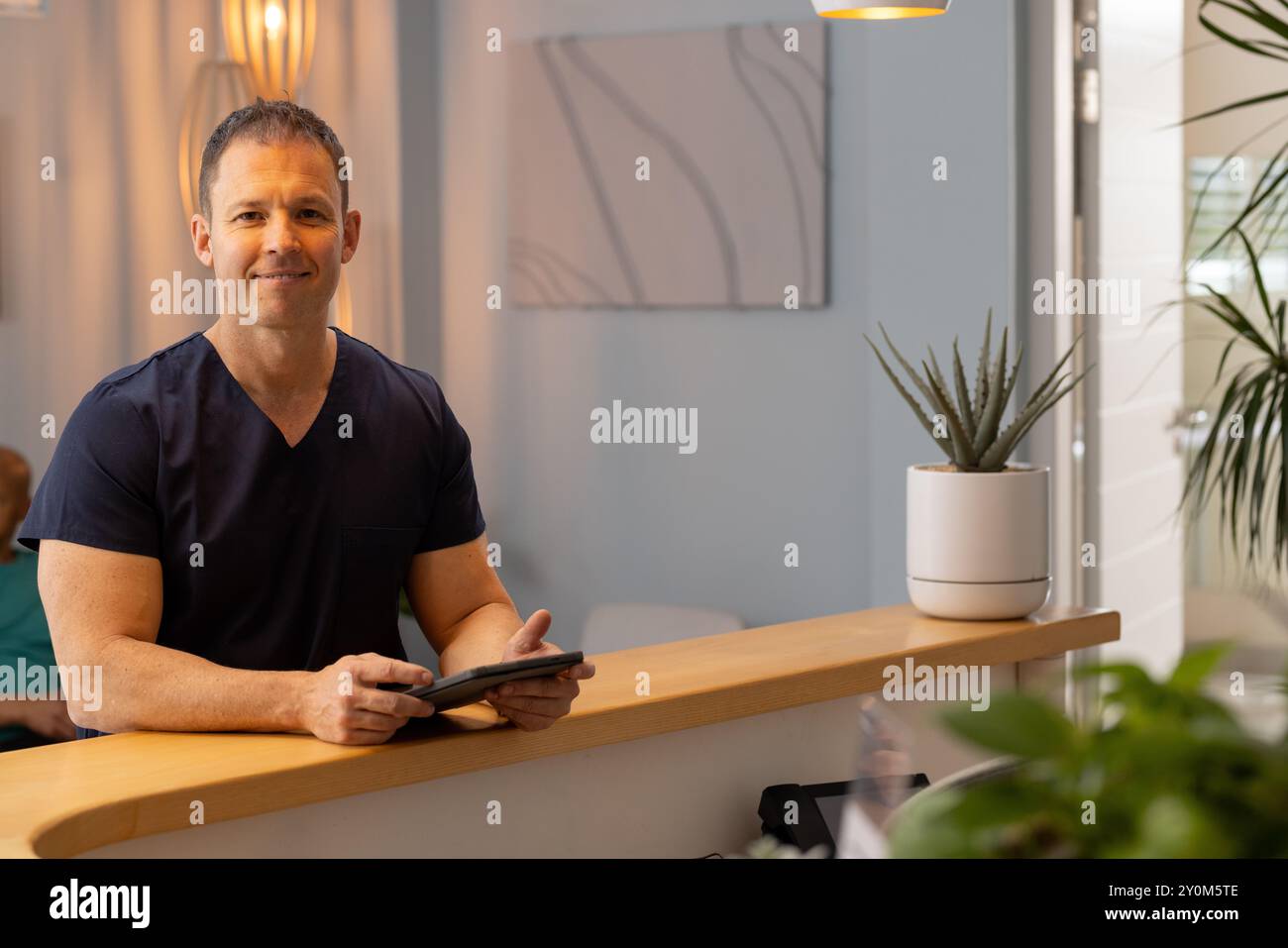 Tenant la tablette, médecin masculin, travailleur de la santé dans les gommages souriant à la réception dans la clinique, espace de copie Banque D'Images