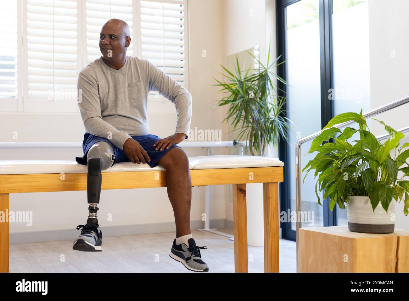 Assis sur banc, homme avec jambe prothétique souriant dans un centre de rééducation. Soins de santé, physiothérapie, récupération, prothèses, patient, bien-être Banque D'Images