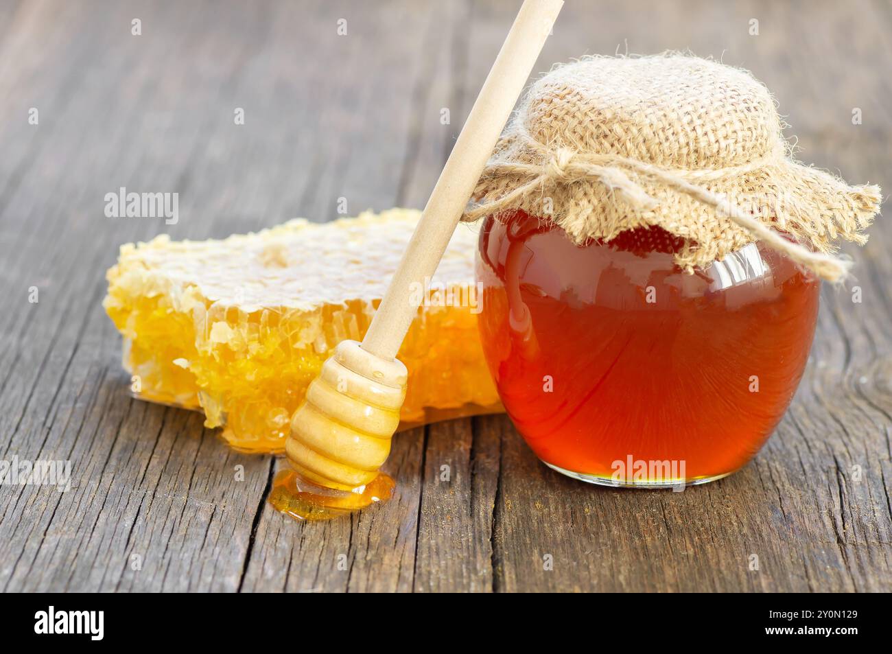 Morceau de nid d'abeille, miel liquide frais organique dans un pot en verre avec un plongeur sur fond en bois, nourriture saine Banque D'Images