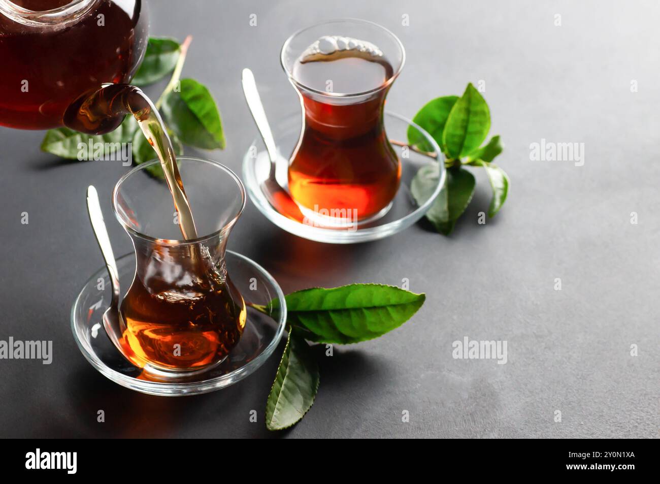 Tasse en verre de thé noir coulant de la théière avec des feuilles de thé fraîches, boisson chaude traditionnelle turque infusée Banque D'Images