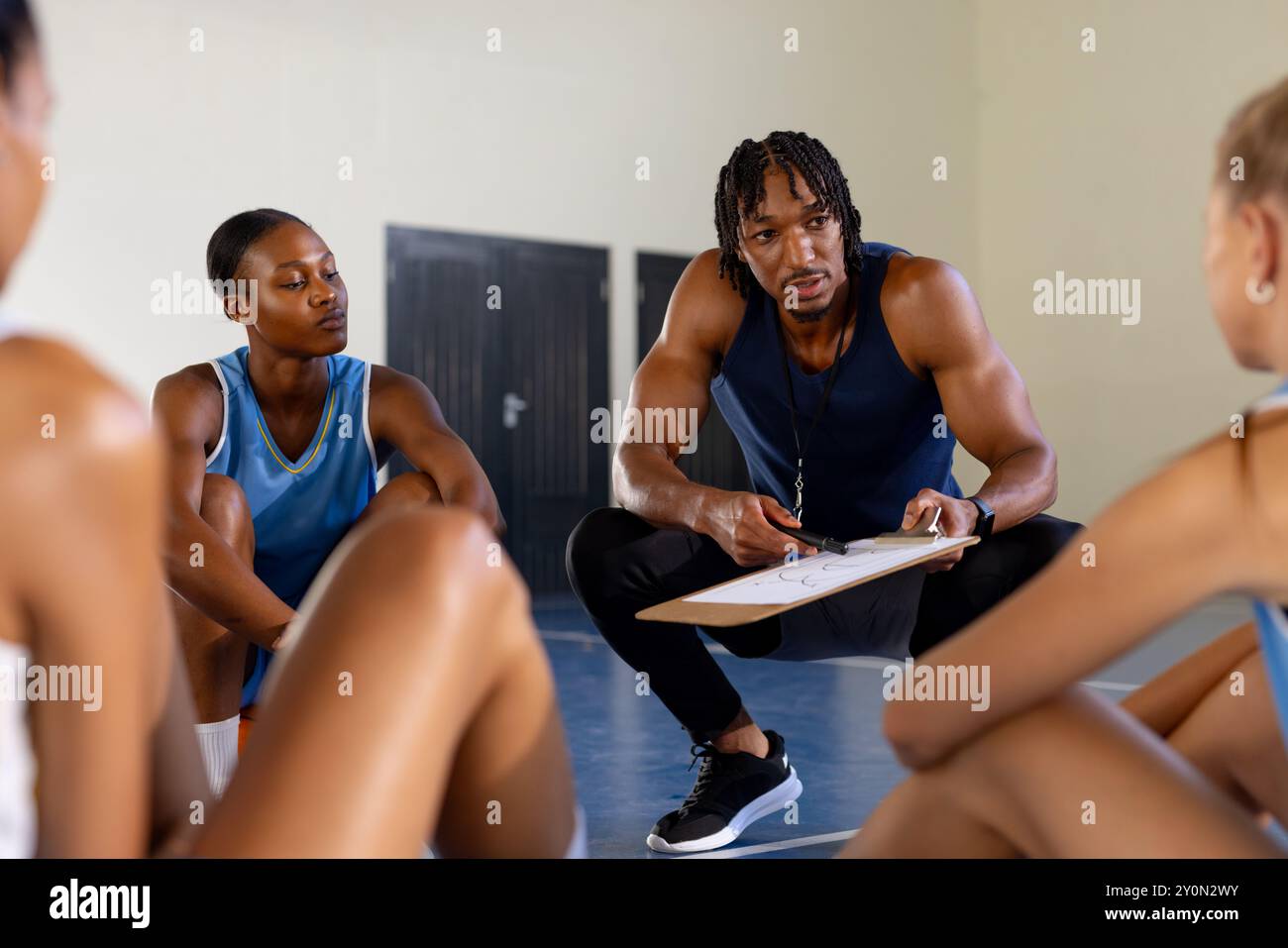 Entraîneur masculin de basket-ball discutant de stratégie de jeu avec des joueuses dans le gymnase Banque D'Images
