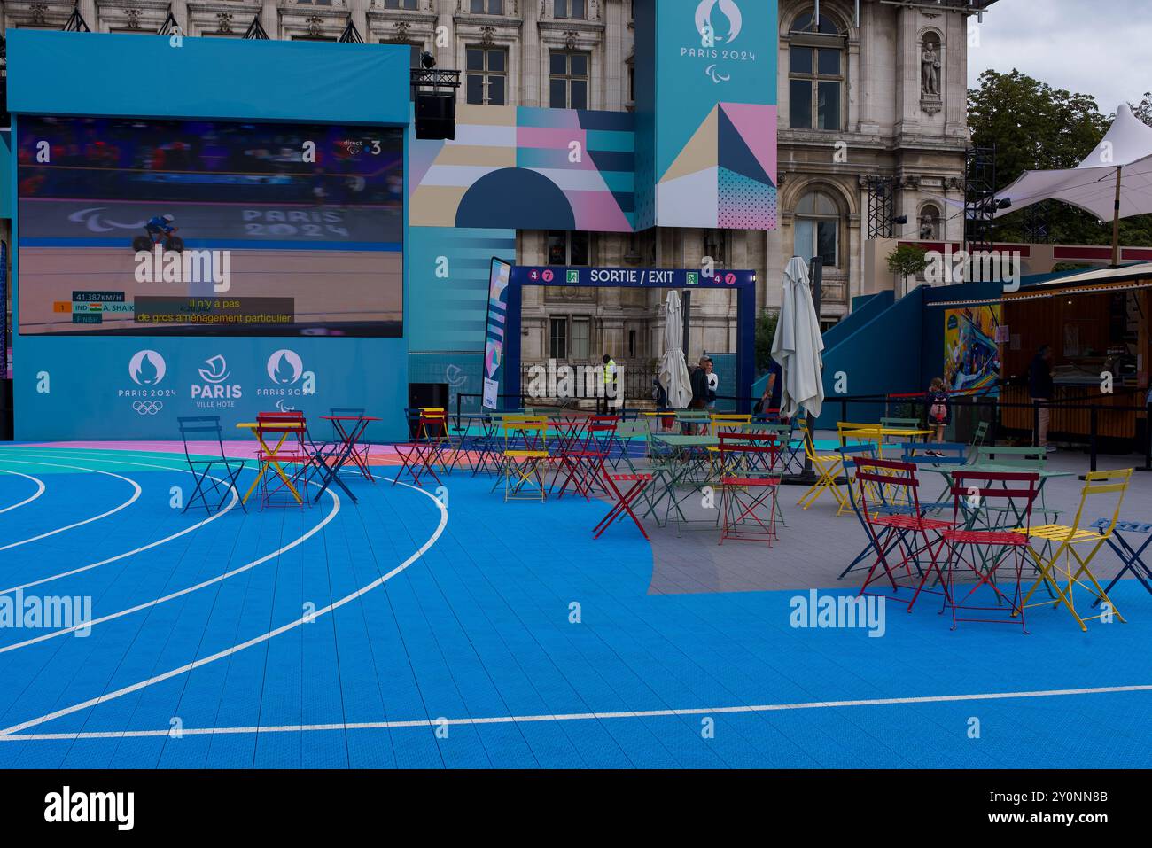 Paris 2024. Tôt le matin dans la zone des fans des Jeux Paralympiques. Chaises de jardin françaises vides colorées sur la piste de course avec un grand écran. Banque D'Images