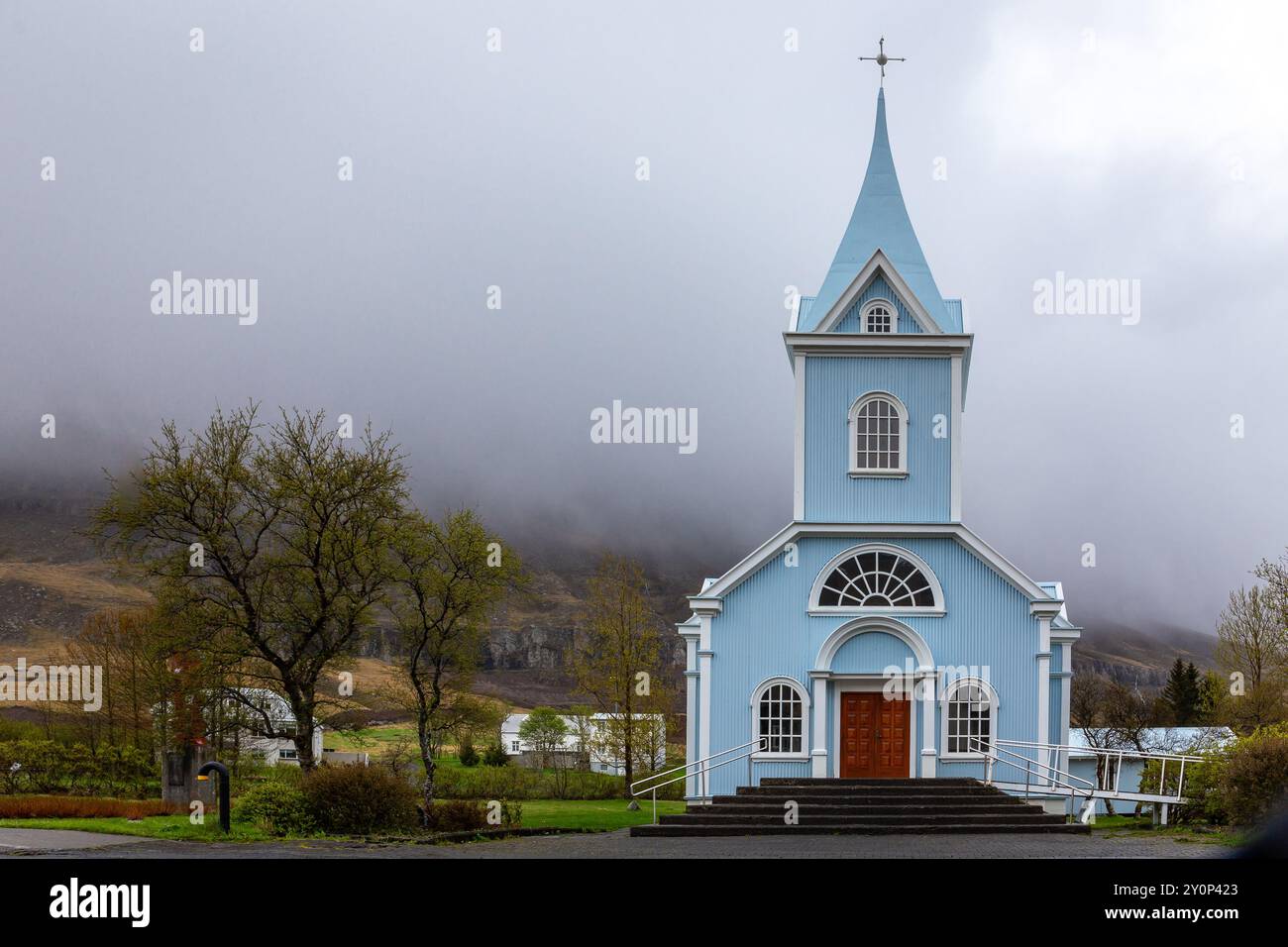L'église bleue de Seydisfjordur (Seydisfjardarkirkja), vue extérieure de la façade du bâtiment bleu vif, montagnes brumeuses en arrière-plan, Islande. Banque D'Images