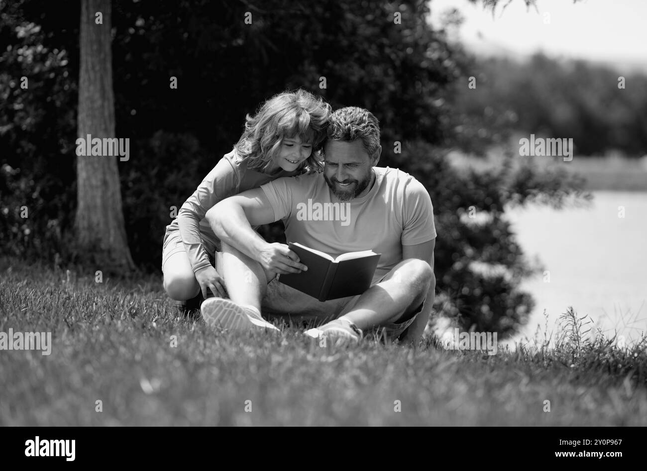 Une famille charmante lisant un livre sur l'herbe. Un garçon et un père pique-nique dans le parc. Un fils heureux et un père lisant un livre. Famille du bonheur. Père lisant un Banque D'Images