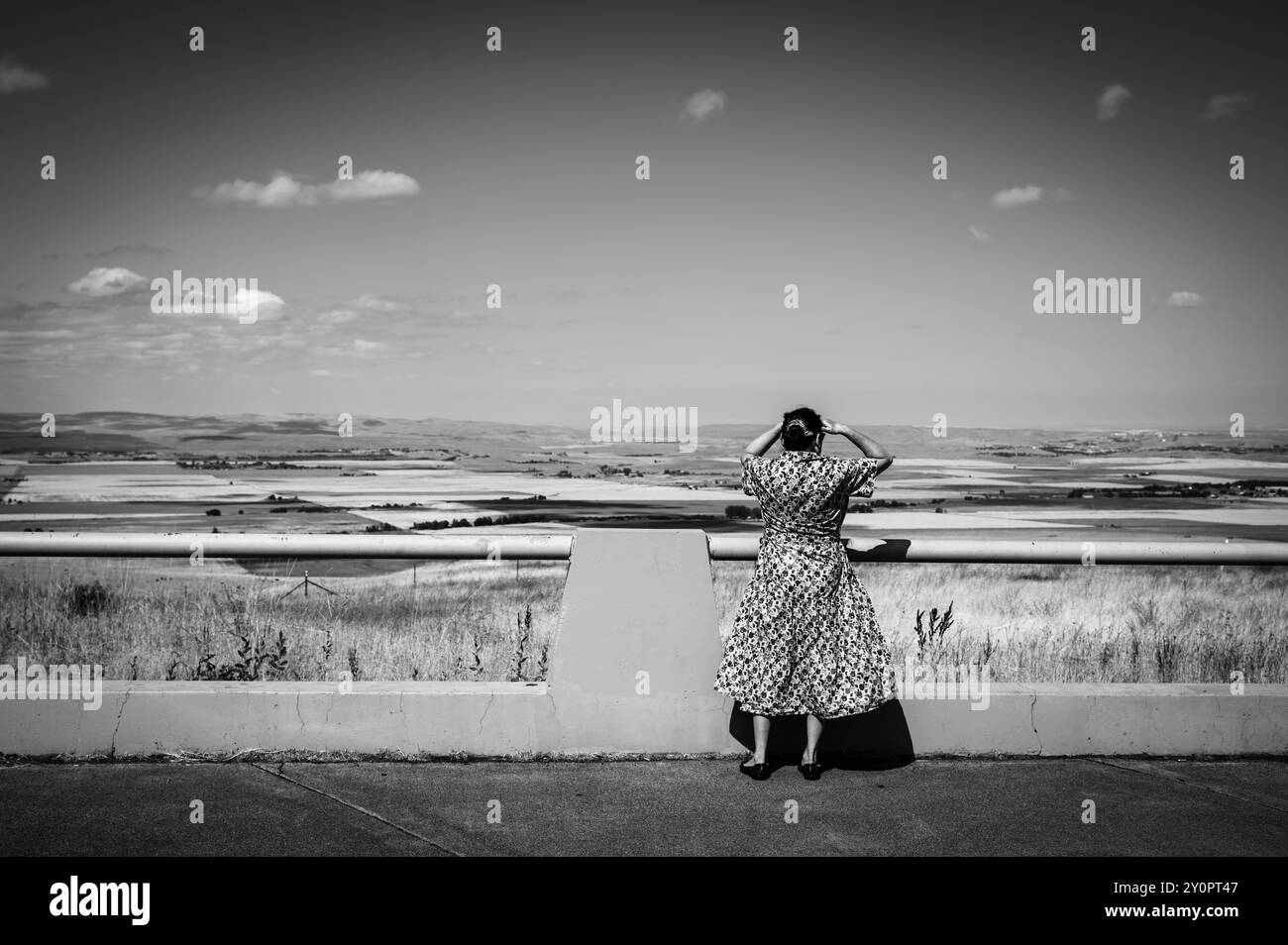 Une femme regarde la prairie de l'Oregon et les terres agricoles depuis un arrêt de repos sur l'autoroute. Champs de blé jaune, ciel bleu et robe bleue. Noir et blanc im Banque D'Images