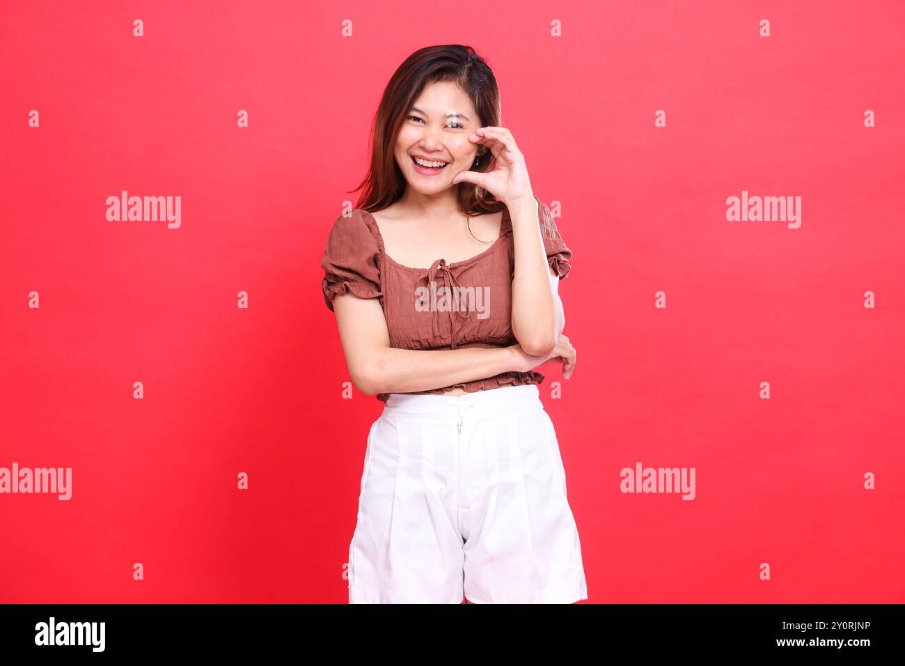 indonésie expression de femme, souriante, croisant les bras en signe d'amour, portant une blouse marron et un short sur fond rouge. pour la mode, la vie Banque D'Images