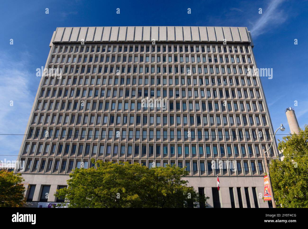 Un immeuble de bureaux moderne de plusieurs étages avec des fenêtres uniformes en forme de grille domine le cadre. La structure en béton se dresse contre un ciel bleu vif. Banque D'Images