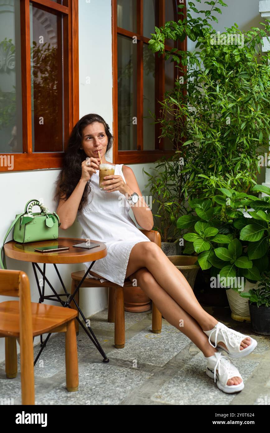 Portrait d'une femme russe de 39 ans sans maquillage assis avec un verre de café glacé en robe blanche Banque D'Images