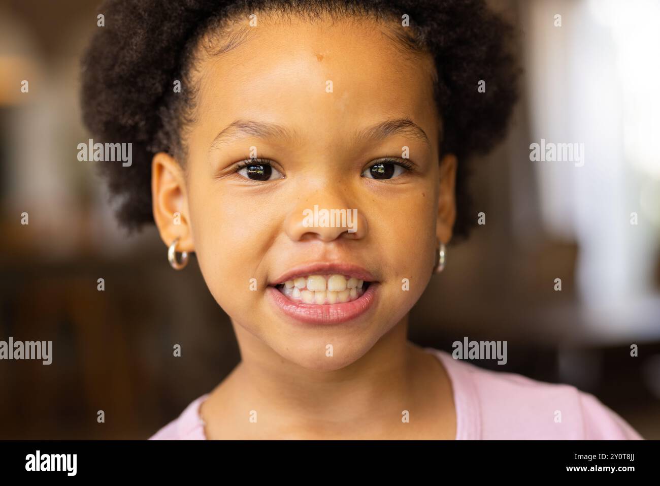 Fille souriante avec des boucles d'oreilles regardant la caméra, portrait en gros plan à la maison Banque D'Images