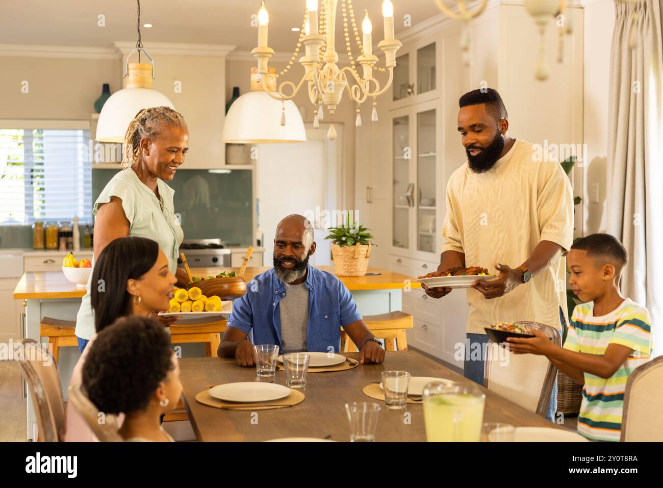 famille multigénérationnelle se réunissant autour de la table à manger, servant de la nourriture et dégustant des repas ensemble Banque D'Images