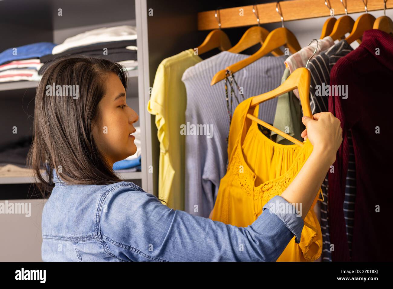 Femme asiatique choisissant la robe jaune de la garde-robe, organisant les vêtements dans le placard Banque D'Images