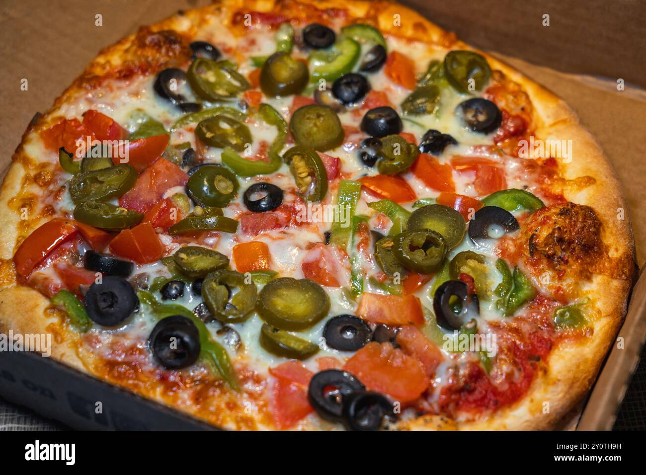 Pizza végétarienne avec olives noires, poivrons verts, tomate et garniture jalapeño dans une boîte à emporter. Banque D'Images