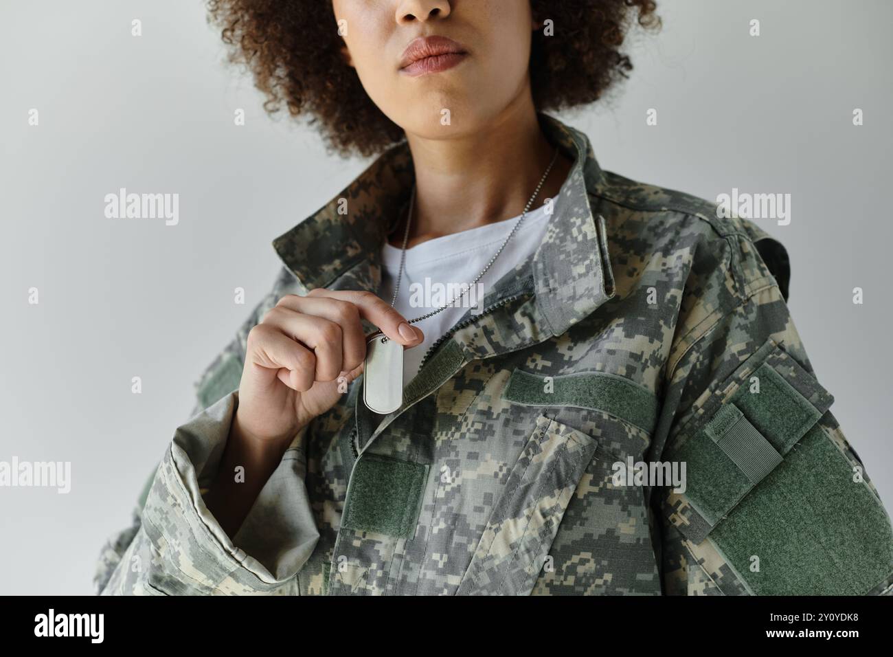 Une jeune femme forte en camouflage militaire tient avec confiance ses étiquettes de chien avec fierté. Banque D'Images