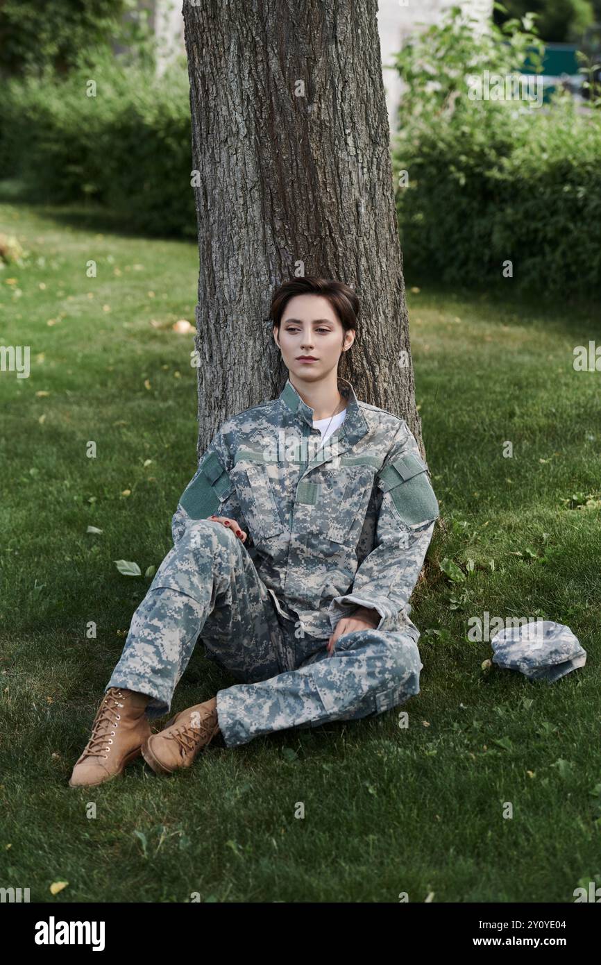 Une jeune femme en camouflage militaire se détend près d'un arbre, réfléchissant sur son retour à la maison. Banque D'Images