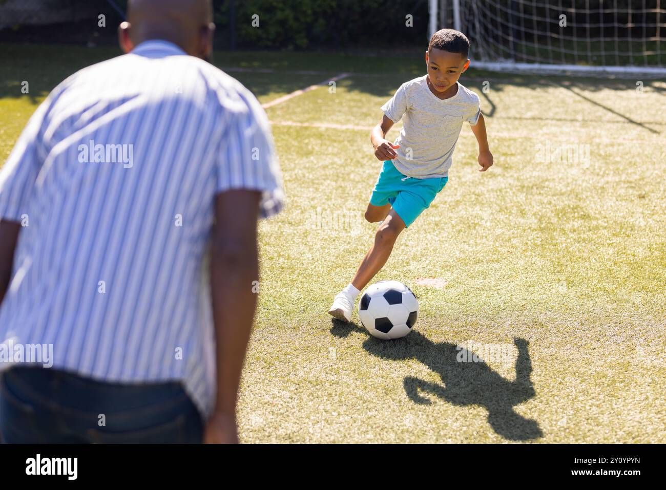 Jouer au football, petit-fils dribble balle sur le terrain avec grand-père regardant attentivement Banque D'Images