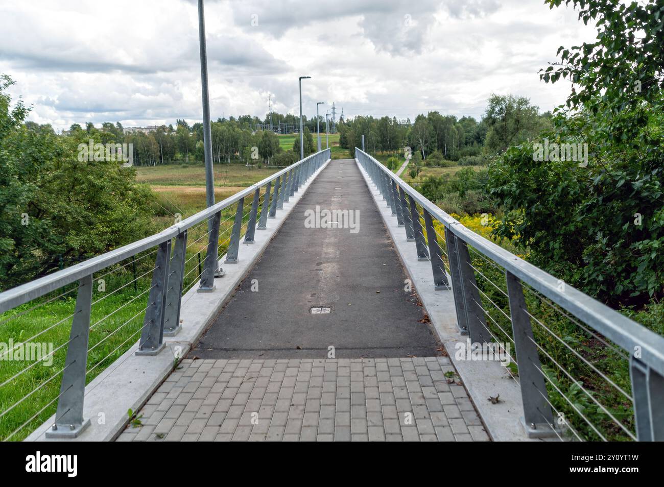 Un large pont piétonnier s'étend sur une verdure vibrante sous un ciel nuageux. Banque D'Images