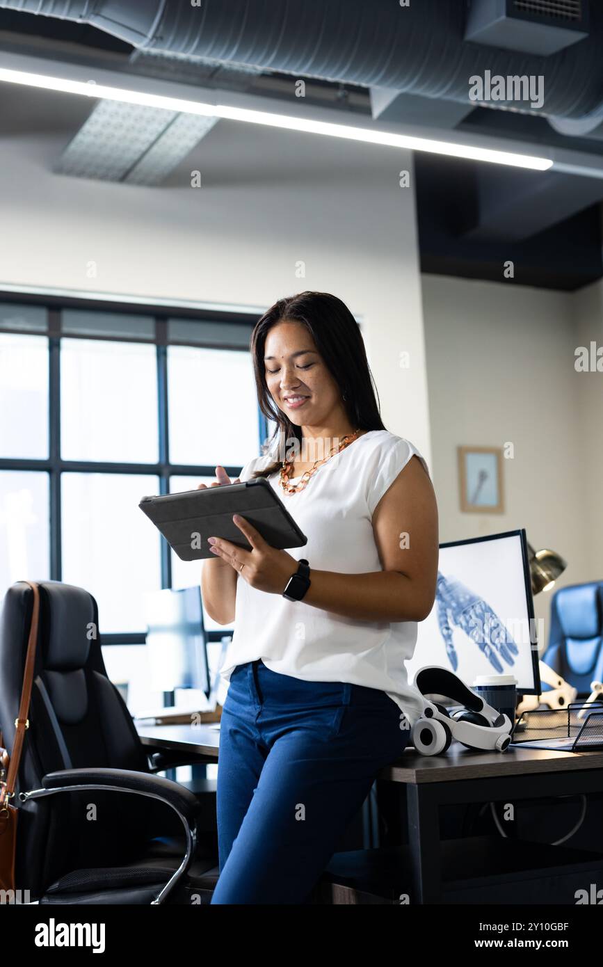 En utilisant une tablette numérique, femme travaillant dans un bureau moderne avec un modèle de main robotique Banque D'Images