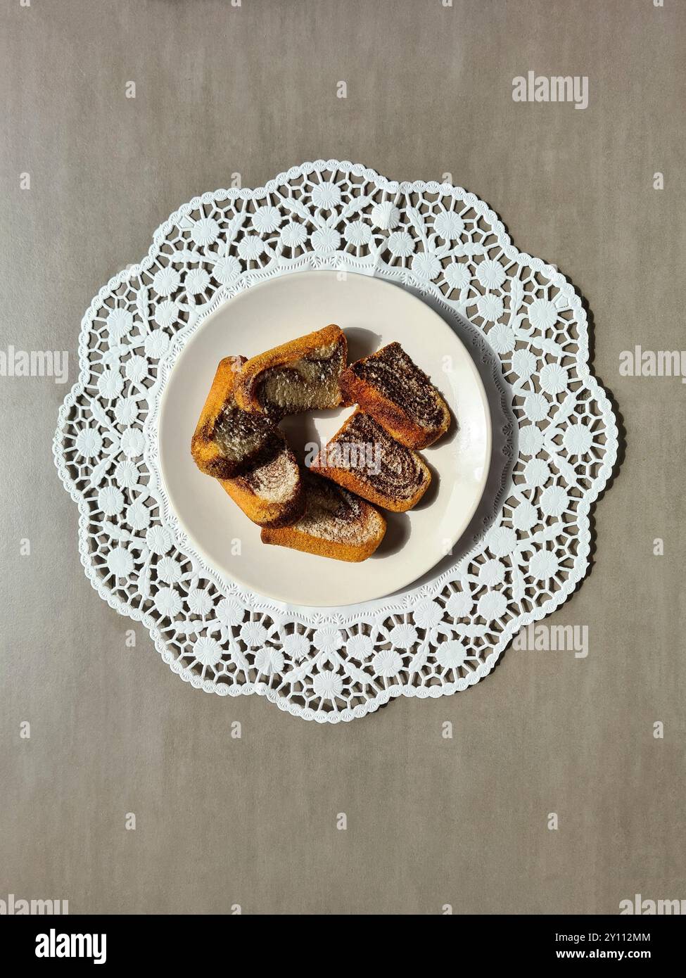 Morceaux individuels de gâteau de marbre servis sur une assiette blanche sur un dessus de gâteau en papier décoratif rond sur un fond gris Banque D'Images