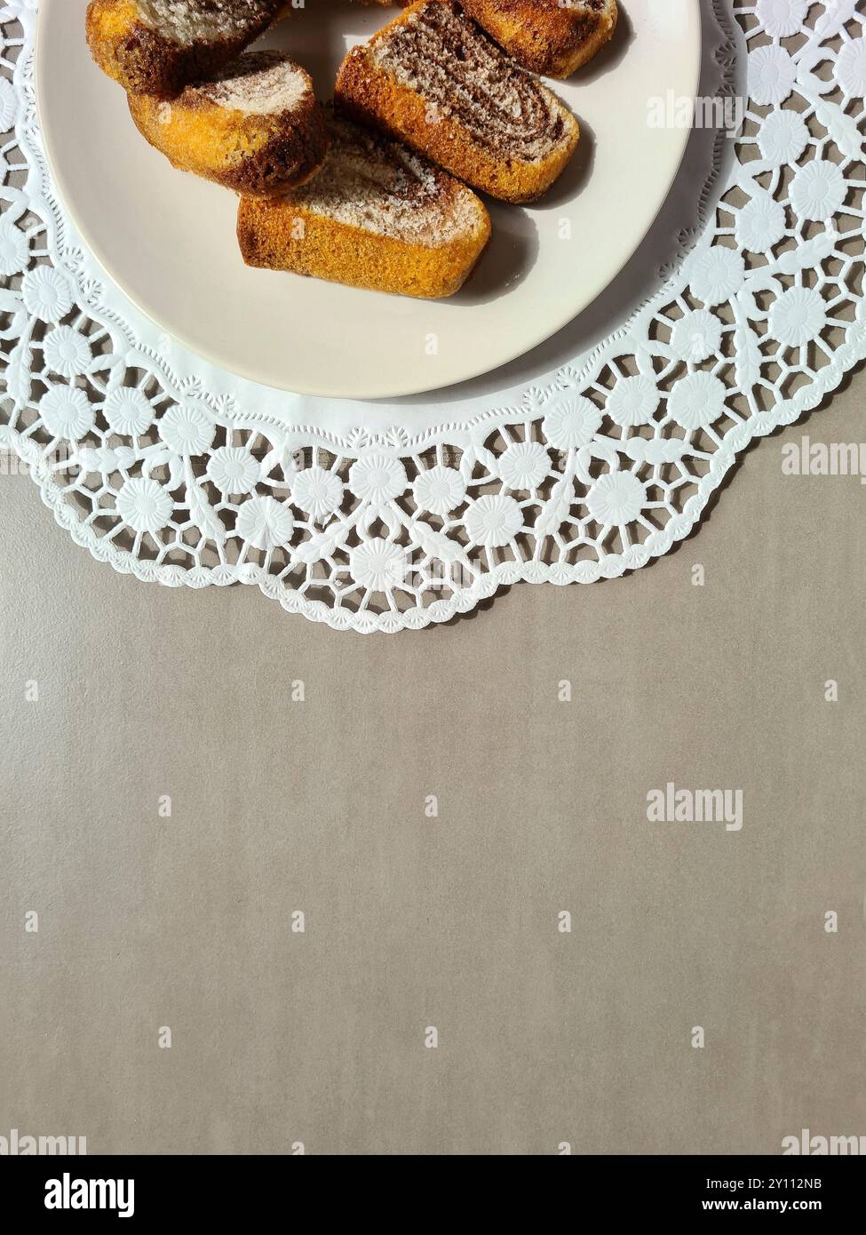 Morceaux individuels de gâteau de marbre servis sur une assiette blanche sur un dessus de gâteau en papier décoratif rond sur un fond gris Banque D'Images