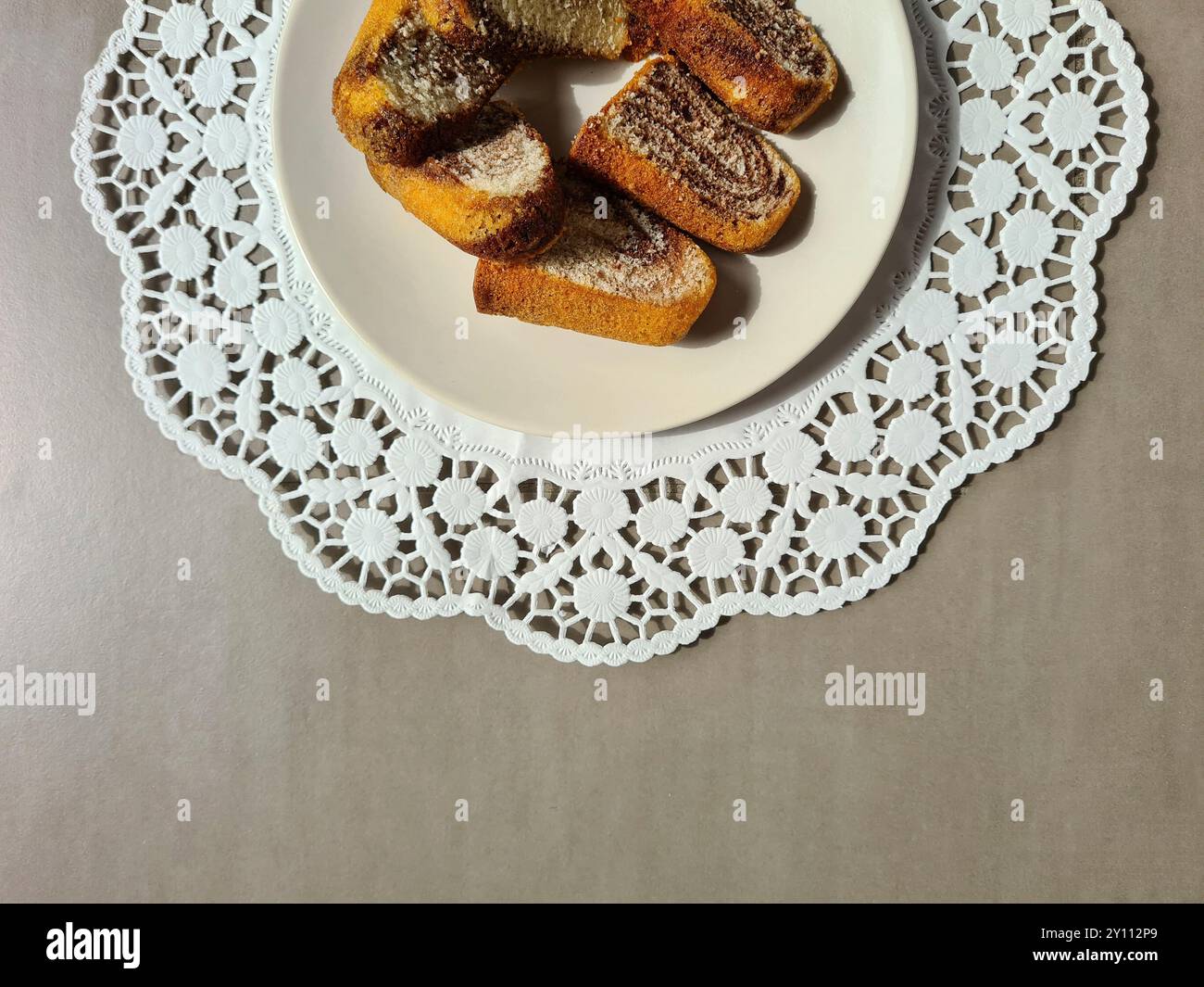 Morceaux individuels de gâteau de marbre servis sur une assiette blanche sur un dessus de gâteau en papier décoratif rond sur un fond gris Banque D'Images