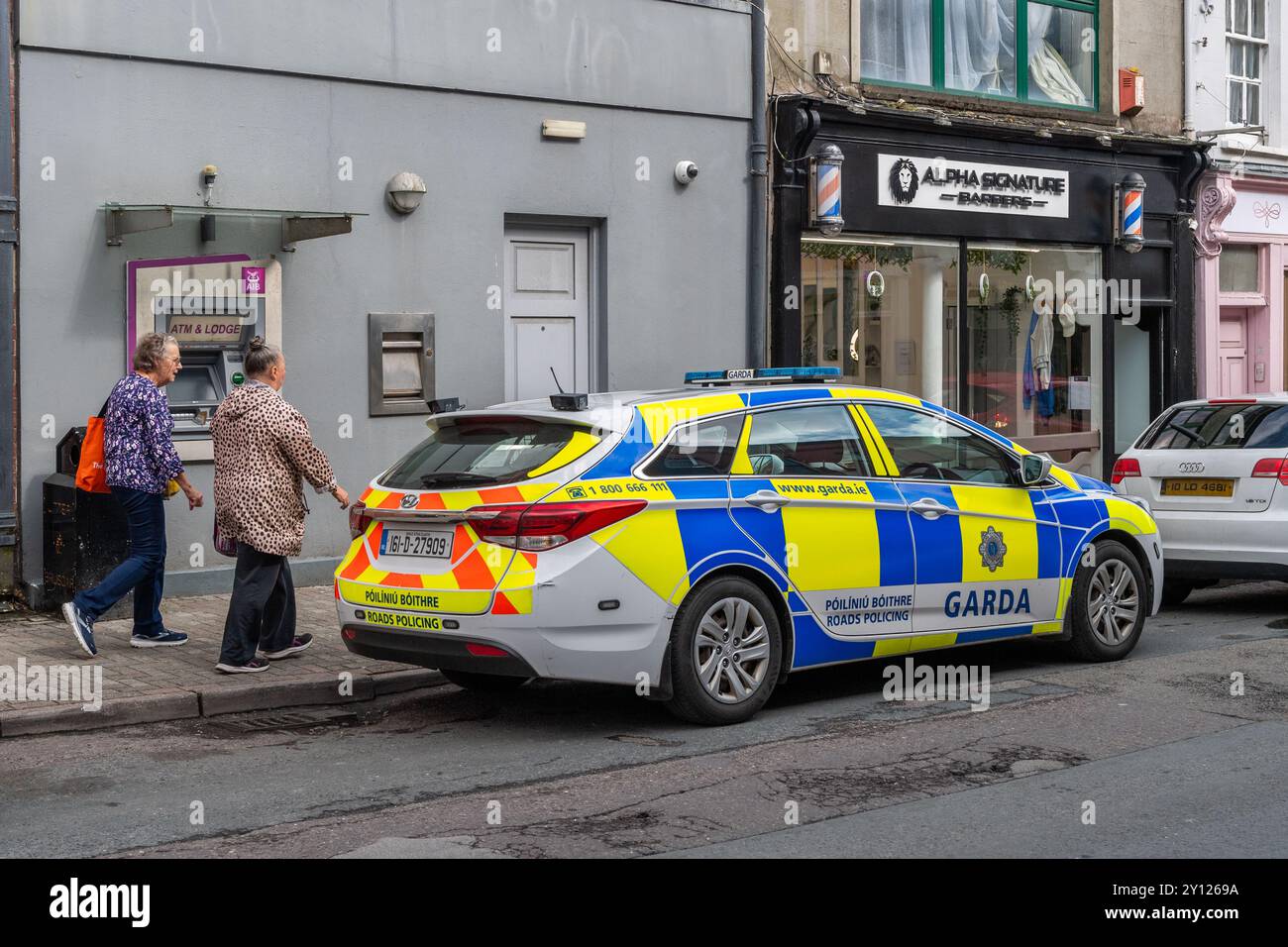 Deux femmes âgées passent devant une voiture de patrouille de la Garda garée à Bandon, West Cork, Irlande. Banque D'Images