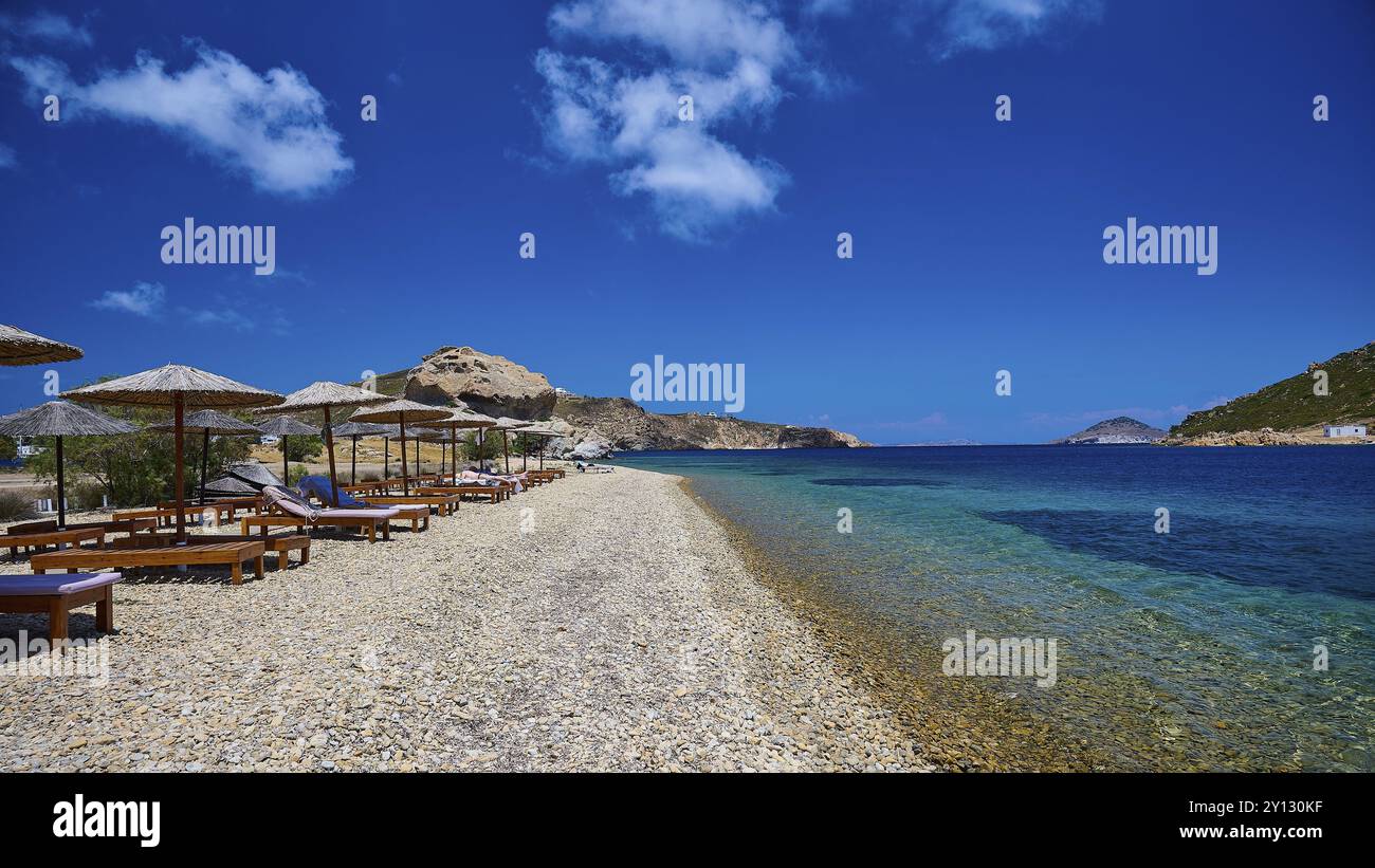 Une plage vide avec transats et parasols de paille sur les eaux bleues claires d'une mer sous un ciel bleu vif, Petras Beach, Kalikatsou Rock, Patmos, D. Banque D'Images