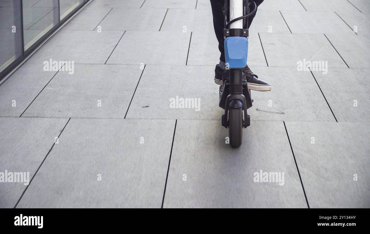 Gros plan sur un trottoir d'une ville d'affaires avec un jeune étudiant en affaires décontracté, homme d'affaires qui monte en scooter électrique Banque D'Images