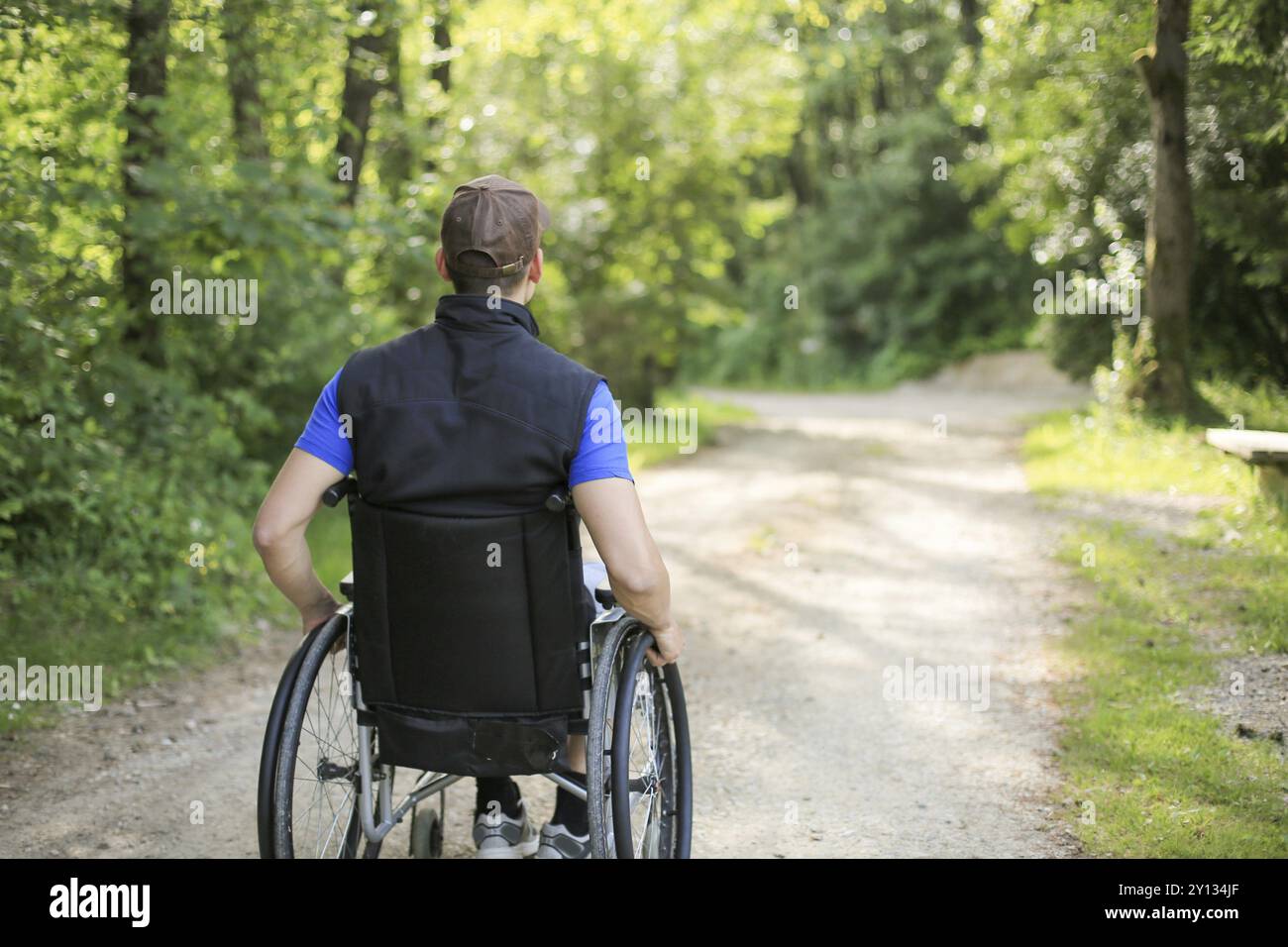 Professionnels et jeunes handicapés homme assis sur un fauteuil roulant dans la nature les roues en rotation sur une route à pied à une belle journée ensoleillée Banque D'Images