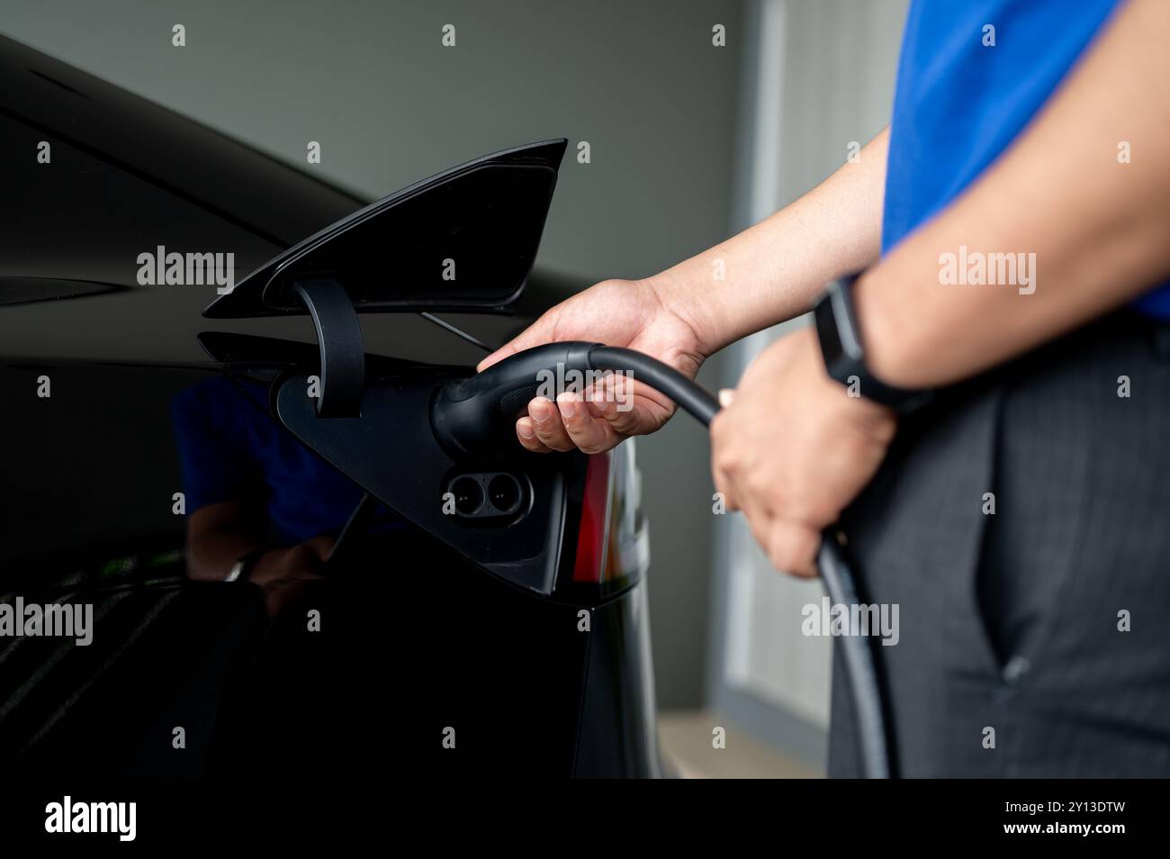 Une image en gros plan d'un homme insérant un câble de recharge dans sa voiture électrique à la maison, la chargeant avant de voyager. technologie verte, vie durable Banque D'Images