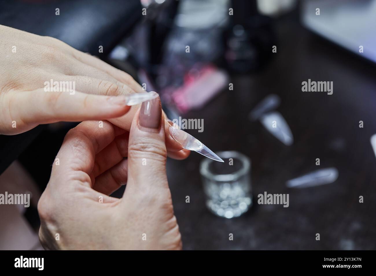 Gros plan d'un technicien en ongles appliquant une extension d'ongle au doigt d'un client dans un salon professionnel. Banque D'Images