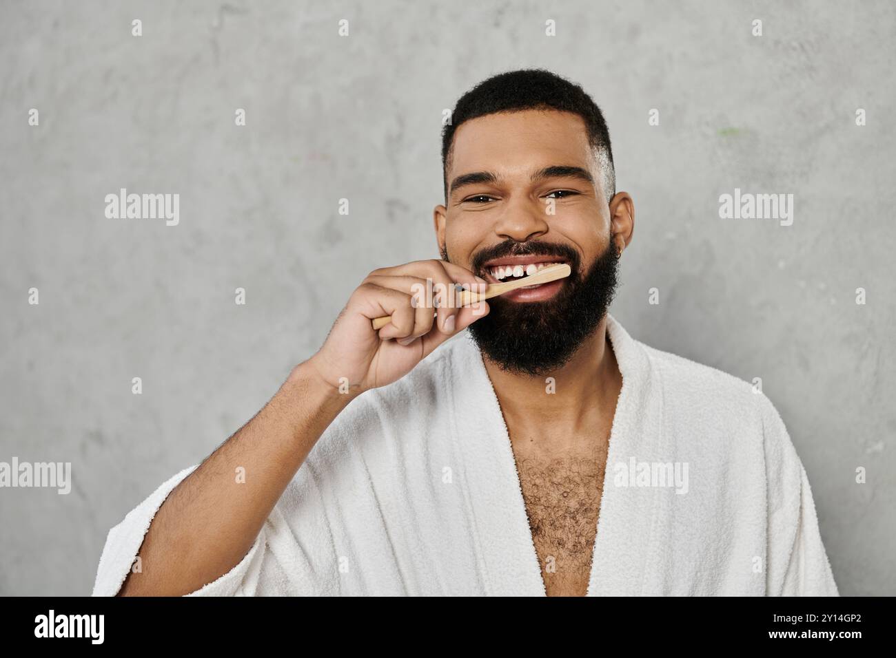 Un homme se brosse les dents, souriant dans une robe douce à la maison. Banque D'Images