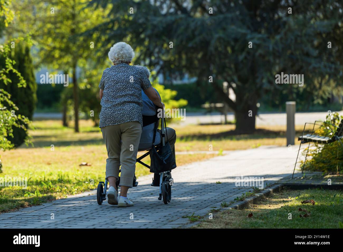 Une femme âgée pousse son mari qui est assis sur un déambulateur Banque D'Images