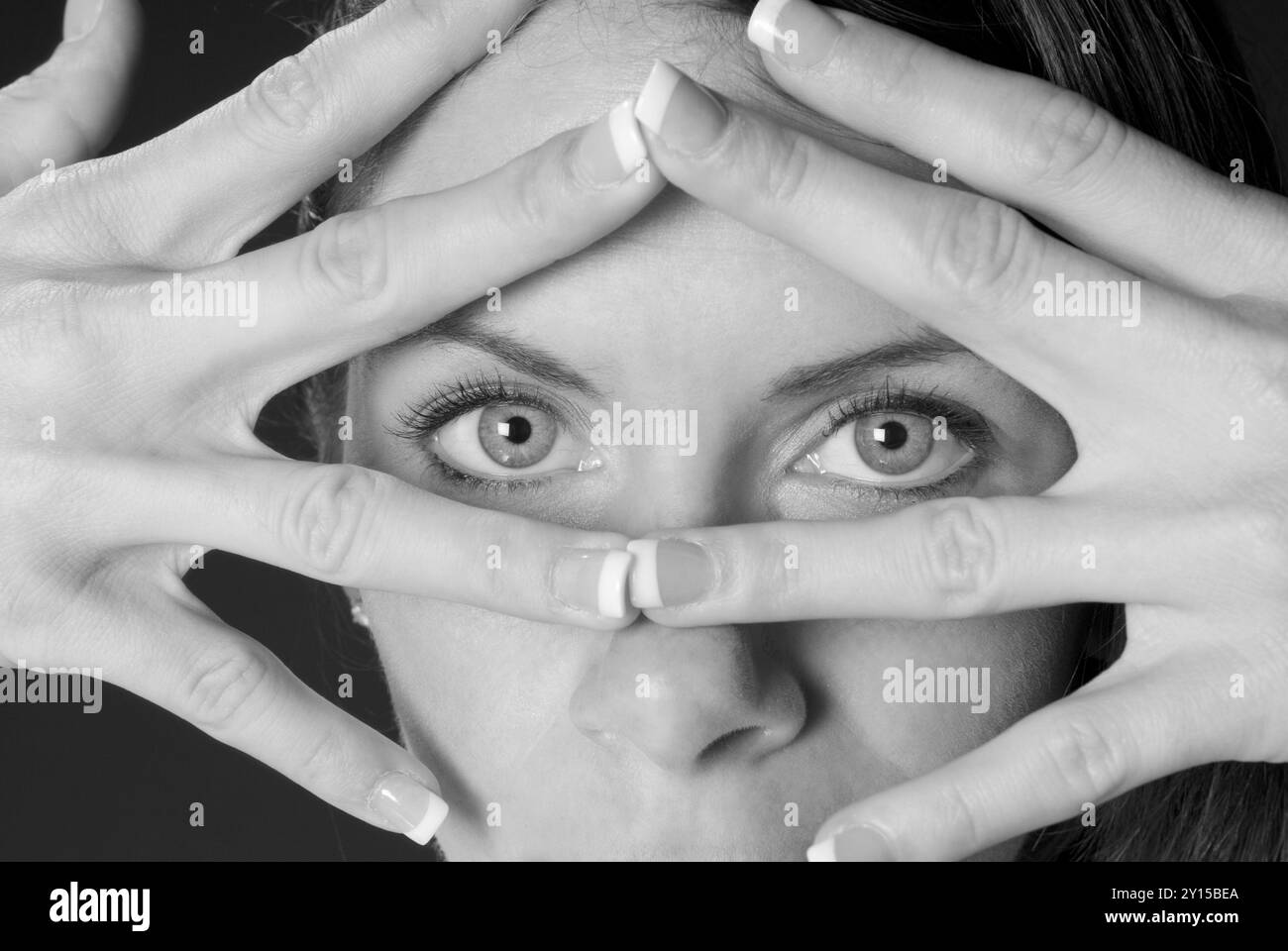 Gros plan d'une belle femme caucasienne, 20 à 25 ans, regardant à travers ses doigts, USA. Banque D'Images