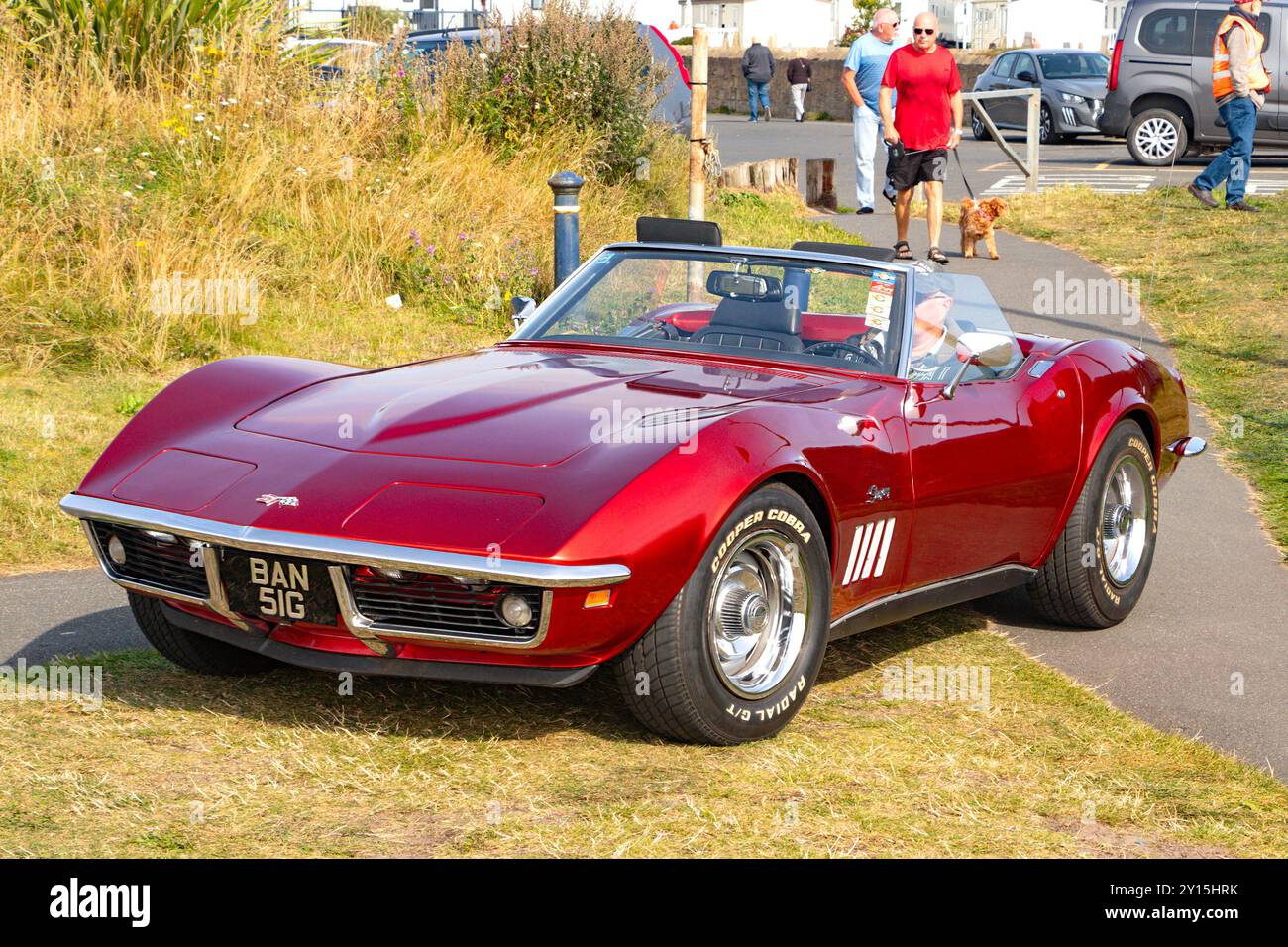 Une voiture sport chevrolet Corvette rouge vintage garée à l'extérieur avec des gens et de la verdure en arrière-plan par une journée ensoleillée. Banque D'Images
