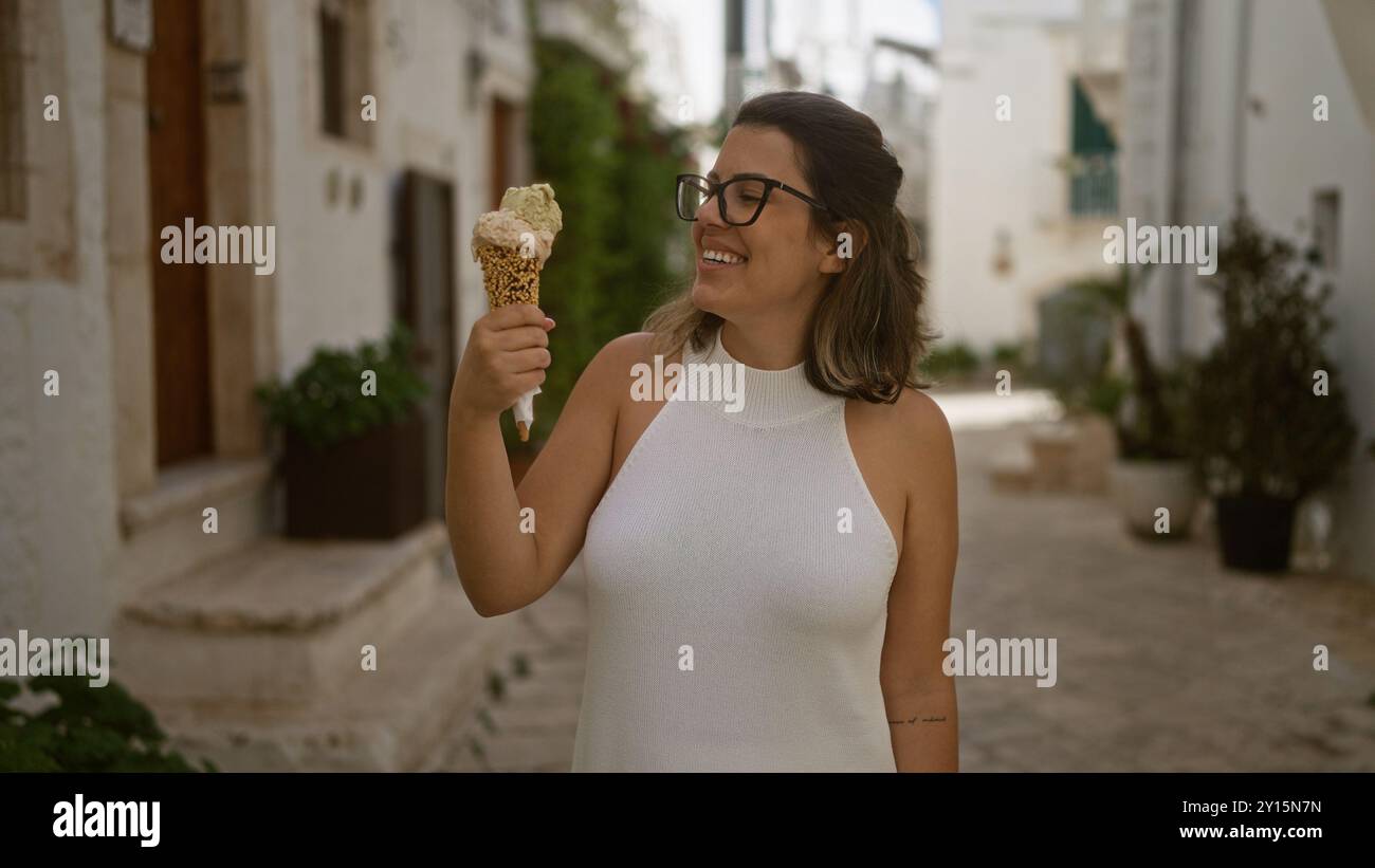 Une belle jeune femme hispanique profitant d'un cornet de crème glacée tout en se promenant dans les charmantes rues blanches de la vieille ville de locorotondo, dans les pouilles, Banque D'Images