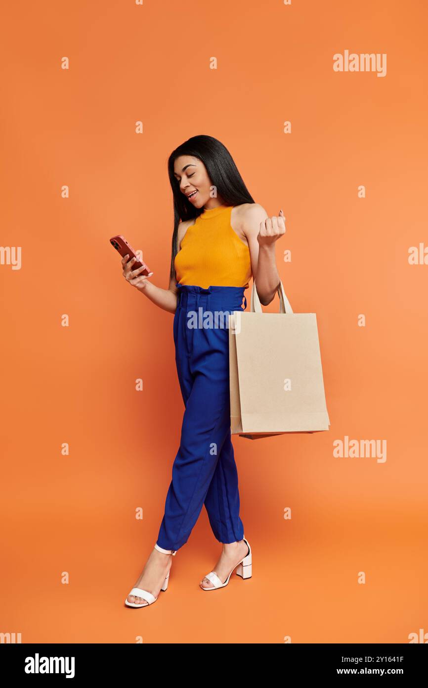 Une femme à la mode vérifie son téléphone tout en transportant des sacs à provisions. Banque D'Images