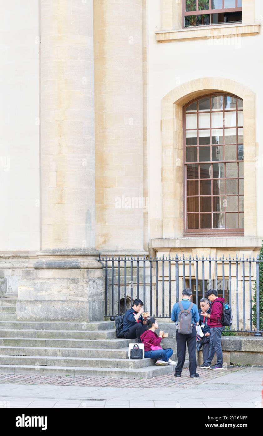 Un groupe de touristes d'outre-mer déjeunent à l'extérieur de l'ancienne bibliothèque, qui fait partie de la bibliothèque Bodleian de l'Université d'Oxford, en Angleterre. Banque D'Images