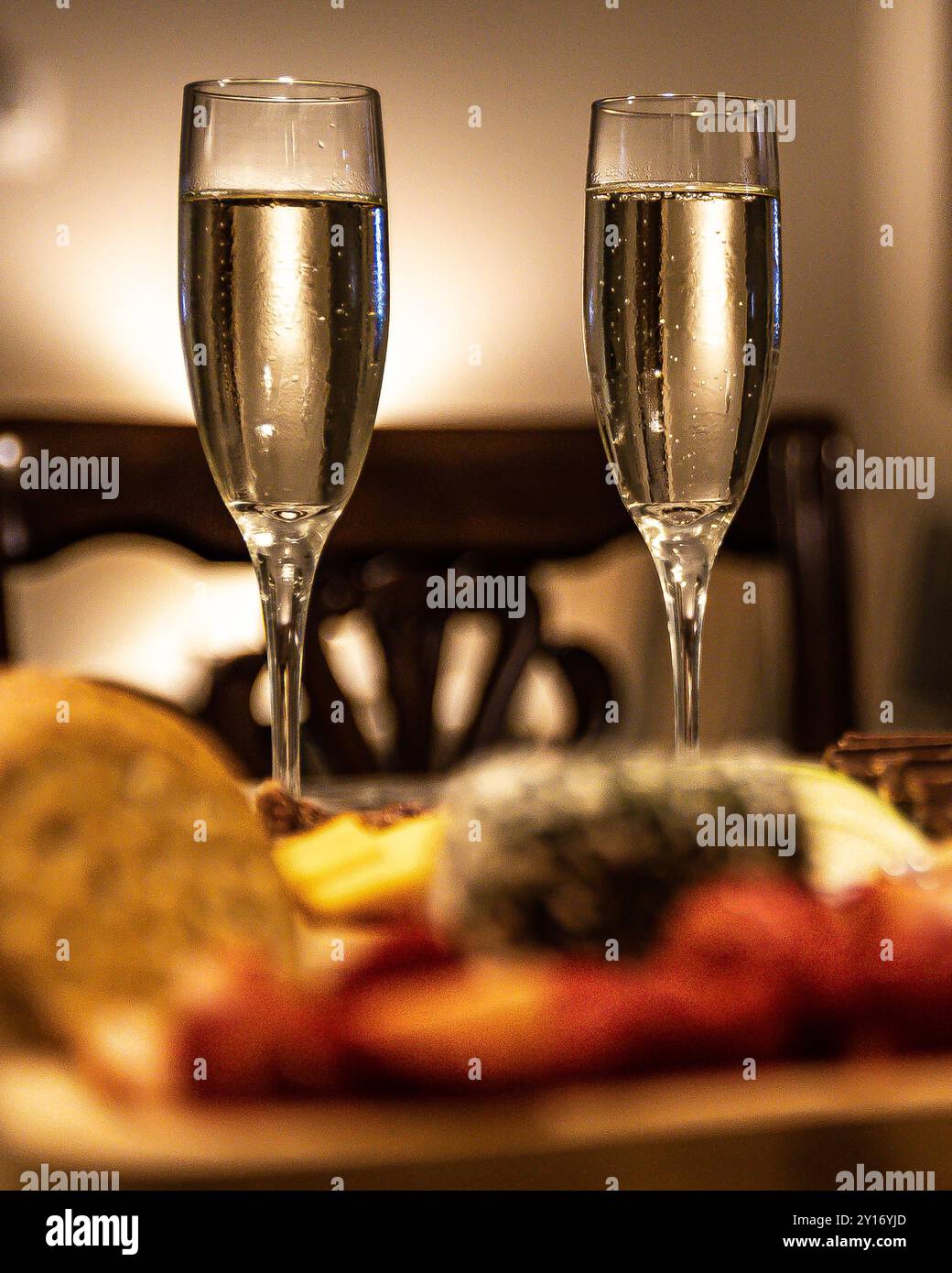 Deux verres de champagne avec plateau de fromage au premier plan et éclairage romantique en arrière-plan Banque D'Images